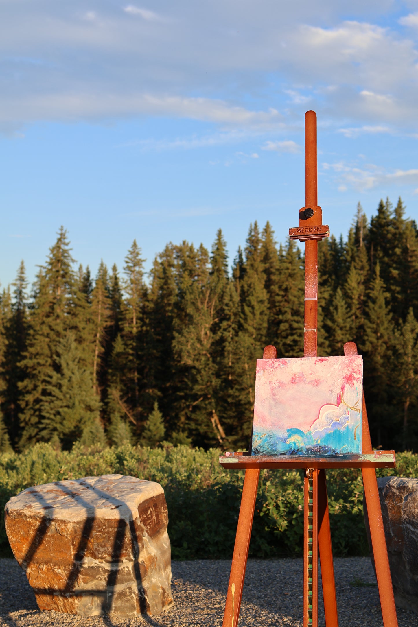 “Edge-less” – original textured abstract painting by Olia Nychyporenko (artbyOliaN), shown outdoors on an easel against a forest backdrop. Acrylic artwork with layered pinks, turquoise, and soft red tones, exploring fluid movement and freedom.