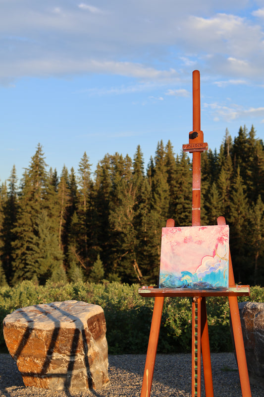 “Edge-less” – original textured abstract painting by Olia Nychyporenko (artbyOliaN), shown outdoors on an easel against a forest backdrop. Acrylic artwork with layered pinks, turquoise, and soft red tones, exploring fluid movement and freedom.