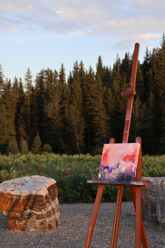 “Ashes and Bloom” – original textured acrylic painting on canvas by Olia Nychyporenko (artbyOliaN), displayed outdoors on an easel against a forest backdrop. Abstract expressionism in warm and deep tones.