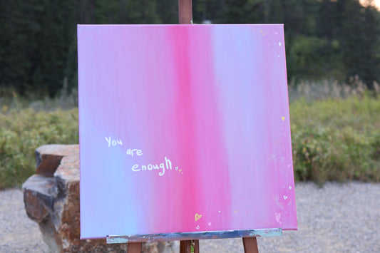 Abstract painting “You Are Enough” – 24x24 acrylic on canvas in pink and soft pastel gradients, with handwritten text “You are enough” and small heart details, displayed outdoors on an easel.